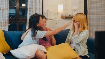 Group of Asian women couple play games at home, female using joystick having funny moment together on sofa in living room in night. Teenager young friend football fan, celebrate holiday concept. photo