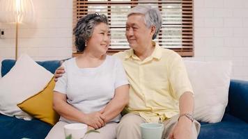 Asian elderly couple feeling happy smiling and looking to camera while relax on the sofa in living room at home. Enjoying time lifestyle senior family at home concept. Portrait looking at camera. photo