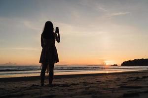 Young Asian woman watching sunset near beach, beautiful female happy relax enjoy moment when sunset in evening. Lifestyle woman travel on beach concept. photo