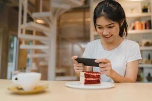 bloguera asiática amigable mujer influyente come pastel en el café de la noche. hermosa jovencita feliz relajarse diversión usando tecnología teléfono móvil tomando una foto de su carga de comida en las redes sociales en el campus universitario.