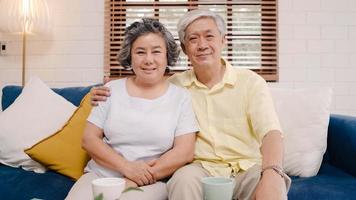 Asian elderly couple feeling happy smiling and looking to camera while relax on the sofa in living room at home. Enjoying time lifestyle senior family at home concept. Portrait looking at camera. photo