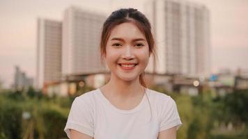 Cheerful beautiful young Asian woman feeling happy smiling to camera while traveling on street at downtown city in the evening. Lifestyle tourist travel holiday concept. Portrait looking at camera. photo