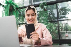 Beautiful young smiling asian muslim woman working on phone sitting in living room at home. Asian business woman working document finance and calculator in her home office. Enjoying time at home. photo