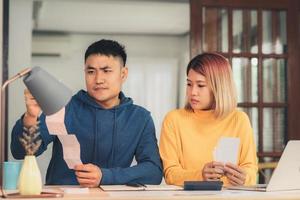 Young stressed asian couple managing finances, reviewing their bank accounts using laptop computer and calculator at modern home. Woman and man doing paperwork together, paying taxes online. photo