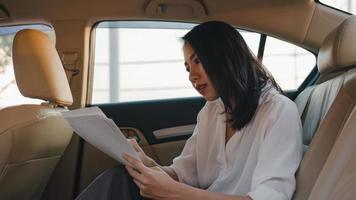 Successful young Asia businesswoman in fashion office clothes working in sitting back seat of car in urban modern city in the morning. Business on the go to work concept. photo