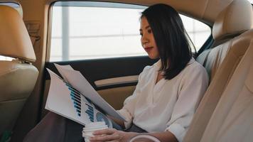 Successful young Asia businesswoman in fashion office clothes working in sitting back seat of car in urban modern city in the morning. Business on the go to work concept. photo