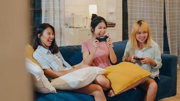 Group of Asian women couple play games at home, female using joystick having funny moment together on sofa in living room in night. Teenager young friend football fan, celebrate holiday concept. photo