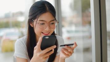 Freelance Asian women online shopping at coffee shop. Young Asia Girl using mobile phone, credit card buy and purchase e-commerce internet on table at outdoor cafe in the evening concept. photo