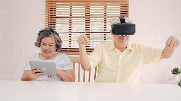 Asian elderly couple using tablet and virtual reality simulator playing games in living room, couple feeling happy using time together lying on table at home. Lifestyle Senior family at home concept. photo