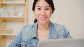 Asia business woman feeling happy smiling and looking to camera while relax at home office. Young asian woman working using laptop on desk in living room at home. photo