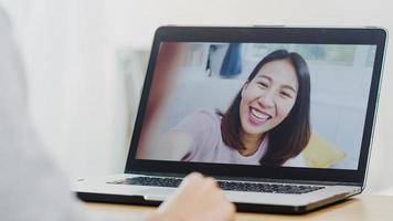 joven mujer de negocios asiática que usa una videollamada portátil hablando con amigos mientras trabaja desde casa en la habitación de la cama. autoaislamiento, distanciamiento social, cuarentena por coronavirus en un nuevo concepto normal. foto