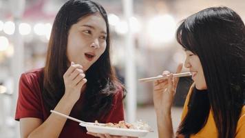 Asian young women friends travel in Bangkok, Thailand, beautiful female feeling happy walking and eating Pad Thai at The Khao San Road. Women travel eat street food in Thailand concept. photo