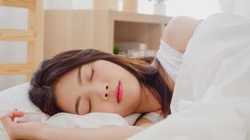 mujer asiática soñando mientras duerme en la cama en el dormitorio, hermosa mujer japonesa usando tiempo de relajación acostada en la cama en casa. mujeres de estilo de vida que usan el concepto de tiempo de relajación en casa. foto