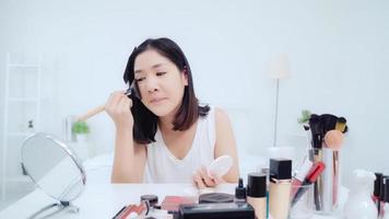 Beauty blogger present beauty cosmetics sitting in front camera for recording video. Happy beautiful young Asian woman use cosmetics review make up tutorial broadcast live video to social network. photo