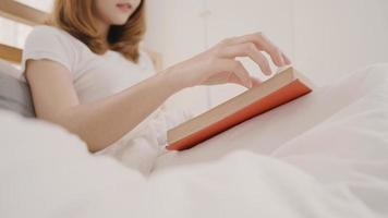 bella y atractiva joven asiática leyendo un libro mientras se acuesta en la cama cuando se relaja en su dormitorio en casa por la mañana. mujeres de estilo de vida que usan el concepto de tiempo de relajación en casa. foto