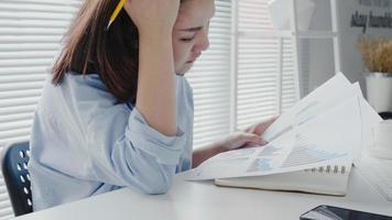 Beautiful young strain asian woman working on laptop while sitting in a living room at home. Asian business woman working in her home office. photo