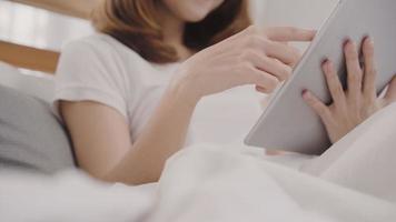 Young Asian woman using tablet while lying on bed after wake up in the morning, Beautiful attractive Japanese girl smiling relax in bedroom at home. Enjoying time lifestyle women at home concept. photo