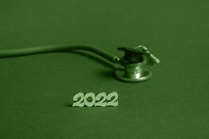 Graduation cap with stethoscope and numbers 2022 on green background, closeup with copy space. Medical education concept. photo