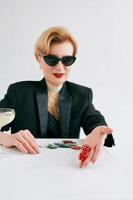 mature stylish woman in black tuxedo and sunglasses with dices in casino. Gambling, fashion, hobby concept. photo