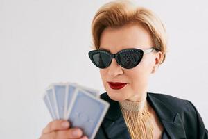 mature stylish woman in black tuxedo and sunglasses in casino. Gambling, fashion, poker face, royal flush, hobby concept. photo