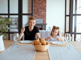 caucasian funny cute siblings -little girl with older brother in dining room in modern loft interior. Family, lifestyle and eating concept photo