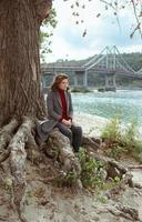 young beautiful brunette depressed sad woman by the river in the city on the bridge photo