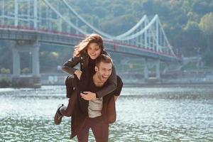 hermosa increíble divertida alegre pareja joven abrazándose al aire libre junto al río en el fondo del puente. novia y novio. concepto de familia, amor y amistad foto