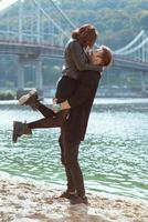 hermosa increíble divertida alegre pareja joven abrazándose al aire libre junto al río en el fondo del puente. novia y novio. concepto de familia, amor y amistad foto