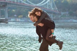 hermosa increíble divertida alegre pareja joven abrazándose al aire libre junto al río en el fondo del puente. novia y novio. concepto de familia, amor y amistad foto