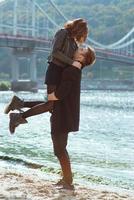 hermosa increíble divertida alegre pareja joven abrazándose al aire libre junto al río en el fondo del puente. novia y novio. concepto de familia, amor y amistad foto