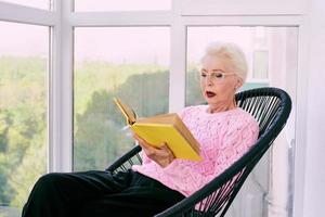 Senior stylish woman sitting on terrace reading book. Education, hobby concept photo