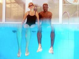 African American man with caucasian woman sitting on the edge of swimming pool. Summer. Vacation, international, and sport concept. photo