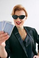mature stylish woman in black tuxedo and sunglasses in casino. Gambling, fashion, poker face, royal flush, hobby concept. photo