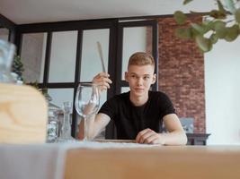 portrait of hungry handsome young man in black t-shirt sitting at the table with fork, knife and empty plate in loft interior indoor photo