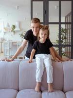 hermanos caucásicos - hermano adolescente y hermana pequeña sentados en un sofá en un moderno interior de loft foto