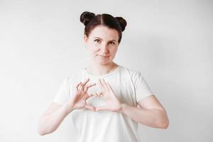 Portrait of beautifull woman with pigtails holding forefinger on her lips while standing over white backgrounnd, asking to keep secret. Copy, empty space photo