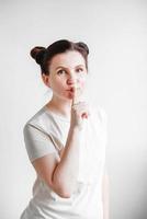 Portrait woman with pigtails holding forefinger on her lips while standing over white backgrounnd. Copy, empty space photo