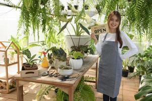 A young woman in an apron holds a welcome open sign in the greenhouse. photo