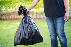Mujer sosteniendo bolsas de basura de plástico negro de basura en el pavimento, concepto de medio ambiente limpio. foto