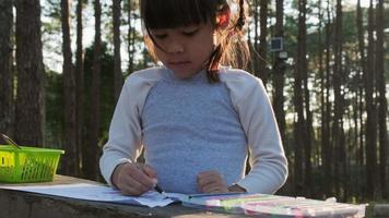 niña coloreando fotos en un camping en un bosque de pinos. Ocio creativo para niños pequeños. los niños pasan tiempo con la familia de vacaciones.