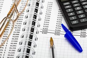 Financial report, pen with cap, calculator, glasses and paper with numbers on the table in the office. A paper sheet full of business data. Accounts number and the data. Business documents. Close-up photo