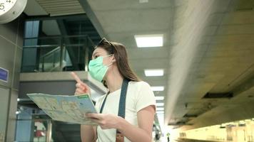 Asian female tourist with face mask, eyeglasses, and camera,  searching traveler location map, looking for destination at Thailand public train station, railway transportation, casual lifestyle. video