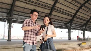 Young couple Asian tourists search information, find travel locations by tablet map at a train station junction in Thailand, passenger holiday trip lifestyle, casual transportation, journey vacation. video