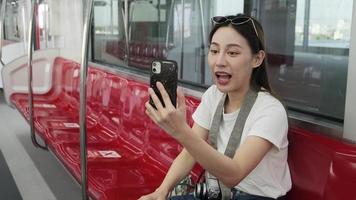 jeune belle touriste asiatique bavardant en ligne, appel vidéo sur téléphone portable, enregistrement et publication sur les réseaux sociaux, transport ferroviaire urbain, mode de vie des passagers de la ville, voyage de vacances heureux. video