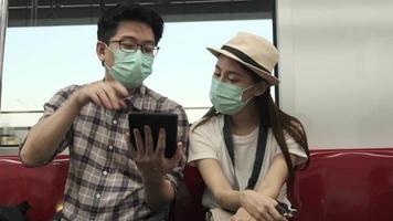 jovem máscara facial casal turistas asiáticos pesquisam informações, encontram locais de viagem pelo mapa do tablet em uma cabine de trem, estilo de vida de viagem de férias de passageiros, transporte casual, viagem de férias na tailândia. video
