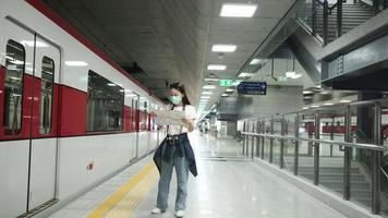 bela turista asiática com máscara facial, óculos e câmera, pesquisando o mapa de localização do viajante, procurando o destino na estação de trem na tailândia, transporte ferroviário, estilo de vida casual. video