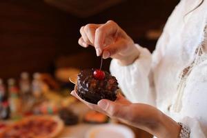 las manos femeninas sostienen un pastel de chocolate con cereza en el restaurante. barra de caramelo enfoque selectivo foto