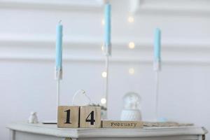 concepto de día de san valentín. fecha 14 de febrero en el calendario de cubos de madera en una caja de regalo blanca y corazón blanco en la mano. bokeh fondo dorado y blanco foto