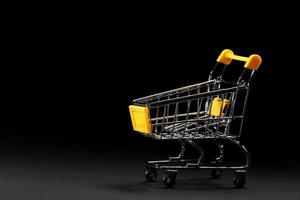 Close up of supermarket grocery push cart for shopping with yellow plastic elements on handle isolated on black background. Concept of shopping. Copy space for advertisement. photo