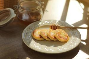 cocina rusa y ucraniana. desayuno. tortitas de requesón o syrniki. pasteles de queso con miel y una cuchara de madera para miel en un plato sobre fondo de madera. enfoque selectivo. foto